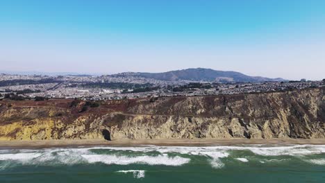 Aerial-View-of-Thornton-beach-Coastal-cliffs-with-turquoise-waves-hitting-the-shore,-drone-pan-right-shot