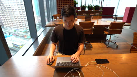 Timelapse,-Chinese-Asian-millennial-with-glasses-sitting-in-front-of-laptop,-working-in-empty-co-working-space