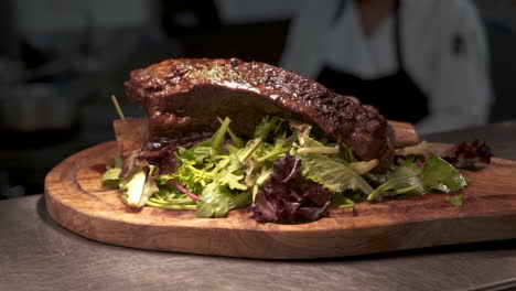 Plated-beef-rib-roast-over-greens-on-wood-carving-board-in-commercial-restaurant-kitchen,-HD