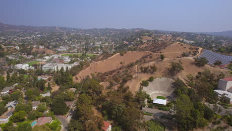 Flyover-Occidental-college-campus-and-Eagle-Rock-neighborhood-and-towards-auditorium,-solar-panels-and-trail-on-top-of-hill-in-Los-Angeles,-California-on-a-beautiful-summer-day