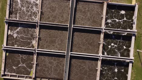 Ascending-top-down-view-of-AySa-water-purification-plant-in-Buenos-Aires,-Argentina-containing-square-pools-of-dirty-water-before-purification