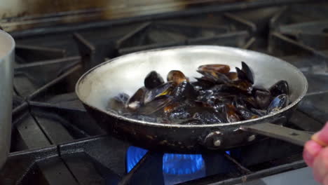 Chef-swirls-mussels-in-pan-over-stove-flame,-cooking-an-order-of-mussels-in-restaurant-kitchen,-slow-motion-HD
