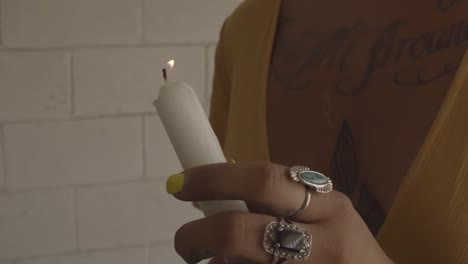 A-young-woman-in-a-yellow-dress-with-a-tattoo-and-rings-lights-a-candle