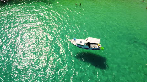 Kleines-Boot,-Das-Auf-Sonnenbeschienenen-Gewässern-Des-Ozeans-Schwimmt,-Mit-Menschen,-Die-An-Einem-Heißen-Tag-Im-Sommer-Am-Prapratno-Strand,-Kroatien,-Schwimmen