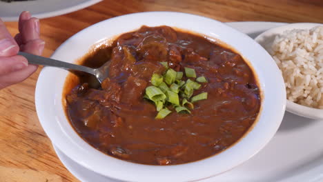 Woman-takes-a-spoonful-of-gumbo,-spoon-scoops-a-biteful-of-dark-rich-cajun-gumbo,-slider-HD