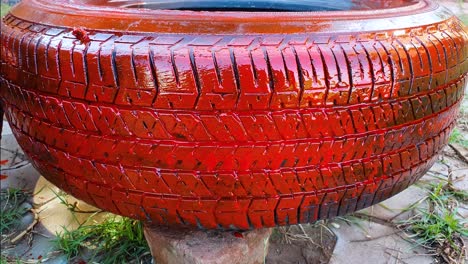 Applying-red-paint-on-old-abandoned-car-tire-for-using-it-as-planter