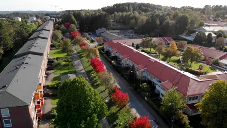 Aufsteigende-Drohnenaufnahme-Einer-Terrassenförmig-Angelegten-Häuserreihe,-Umgeben-Von-Herbstfarbenen-Bäumen