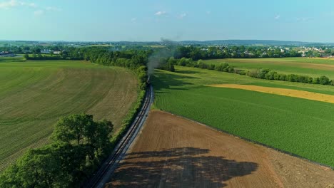 An-Aerial-View-of-a-Steam-Engine-Puffing-Smoke-and-Steam-with-Passenger-Coaches-Traveling-on-a-Single-Track-Thru-Trees-and-Farmland-Countryside-on-a-Beautiful-Late-Afternoon-Golden-Hour-Spring-Day