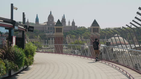 Man-Walking-At-Terrace-Of-Arenas-de-Barcelona-With-Venetian-Towers-And-Palau-Nacional-In-Background-In-Barcelona,-Spain
