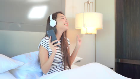 Lächeln-Glückliche-Asiatische-Frau,-Die-Sich-Entspannt-Und-Kopfhörer-Verwendet,-Um-Musik-Vom-Smartphone-Im-Bett-Zu-Hören