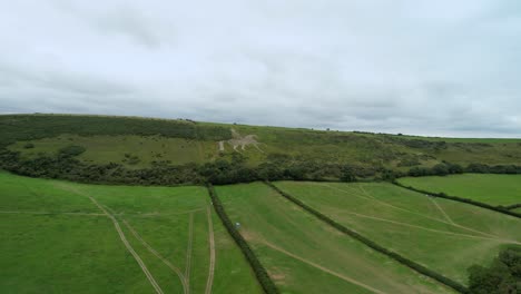 Osmington-White-Horse-limestone-figure-sculpture-on-hillside-farmland-aerial-view-push-forwards