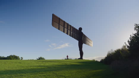 Angel-of-the-North-against-blue-sky,-silhouetted-man-walks-along-the-path