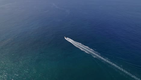 Lone-motor-boat-speeds-across-blue-water,-high-angle-drone-tracking-shot