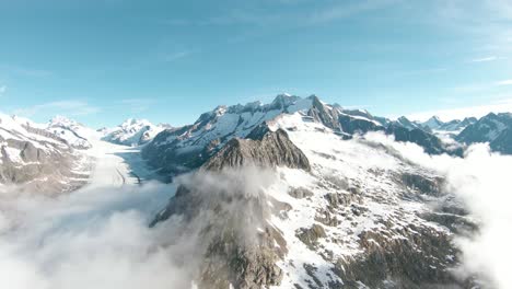 Aerial-drone-fly-over-mountain-tops-and-mountain-ridge-with-FPV-drone-close-to-aletsch-glacier,-Switzerland-above-clouds