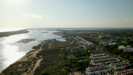 Aerial-Panorama-landscape-view-of-Puerto-Marina-El-Rompido-at-sunset---private-real-estate-houses,-sandy-beachline,-dock-with-boats-on-Piedras-river,-hotels-surrounded-with-Stone-Pines