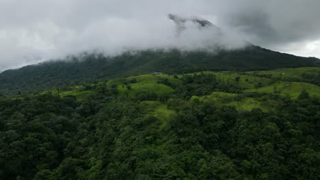 Aerial-view-moving-away-shot,-Scenic-view-of-the-rain-forest-on-the-foot-hill-of-Arena-Volcano-in-Costa-Rica,-cloudy-sky-in-the-background