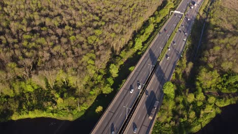 Aerial-view-of-dynamic-movement-of-vehicles-on-interstate-expressway-amidst-beautiful-greenery-during-sunset