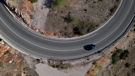 Black-car-driving-on-curve-of-mountain-road,-top-down-zoom-aerial-view,-travel-concept