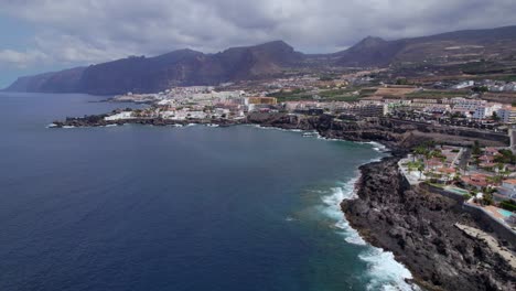 Flying-along-rocky-shore,-Puerto-de-Santiago-near-Los-Gigantes,-Tenerife,-drone-establishing-shot