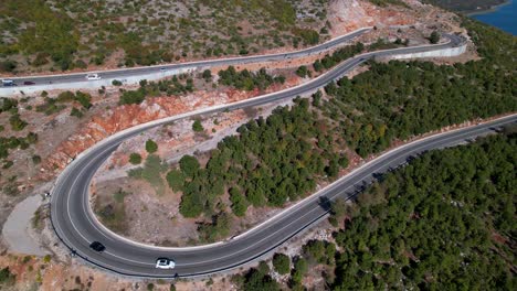 Cars-driving-on-winding-panoramic-road-near-beautiful-lake,-circle-aerial-shot