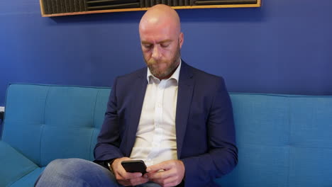 Business-man-looking-and-browsing-on-mobile-cell-phone-while-sitting-on-sofa