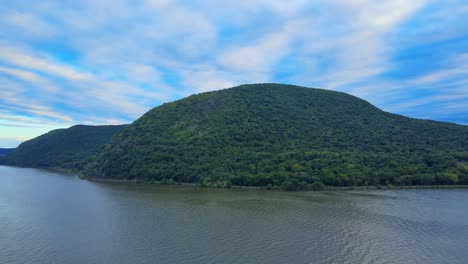 Aerial-drone-footage-descending-on-the-Hudson-River-in-New-York's-Hudson-Valley-with-Storm-King-Mountain-in-the-background-at-sunset