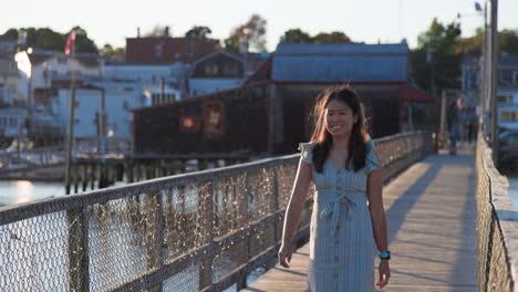 Beautiful-Chinese-girl’s-smile,-walks-on-wooden-harbor-bridge,-at-sunset