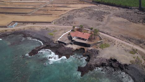 Lone-Spanish-villa-on-barren-rocky-sea-shore,-high-angle-drone-view