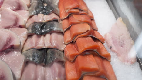 Verschiedene-Fischsorten-In-Der-Vitrine-Des-Meeresfrüchtemarktes,-Frische-Rohe-Fischfilets,-Ordentlich-Auf-Eis-Gestapelt-In-Der-Vitrine-Des-Fischhändlers,-Dolly-Out-HD