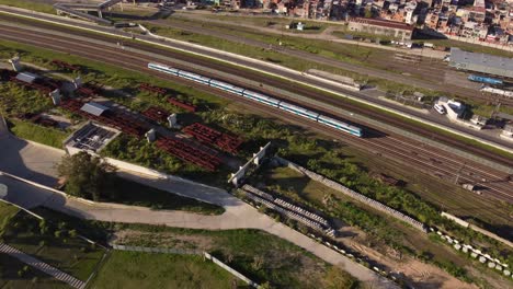 Aerial-top-down-view-of-commuter-train-running-on-track-and-approaching-railway-complex