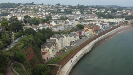 Revealing-aerial-shot-of-Dawlish-town,-along-the-Devon-coast-with-the-railway-track-and-buildings-in-shot