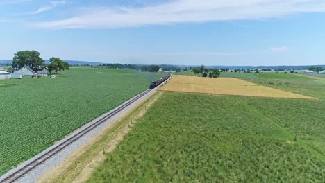 An-Aerial-View-of-a-Steam-Engine-Puffing-Smoke-and-Steam-with-Passenger-Coaches-Traveling-on-a-Single-Track-Fertile-Farmland-and-Countryside-on-a-Beautiful-Spring-Day
