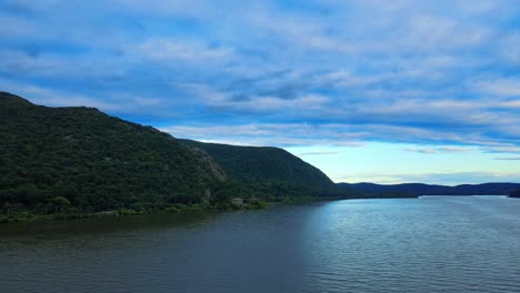 Aerial-drone-footage-rising-over-the-Hudson-River-in-New-York's-Hudson-Valley-with-Storm-King-Mountain-in-the-background-at-susnet