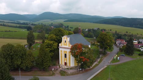 aerial-view-of-a-yellow-country-church-with-graveyard-and-hills-in-the-background-in-Bohemia