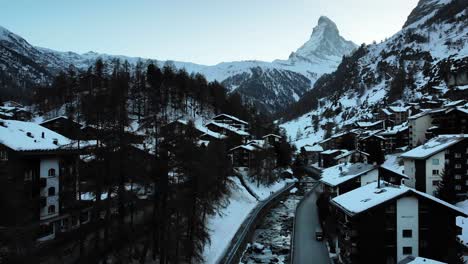 Aerial-flyover-over-Zermatt-alongside-the-river-with-a-view-of-the-Matterhorn-during-a-winter-sunset