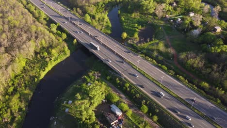 Drone-tracking-shot-of-congested-highway-surrounded-by-green-forest-trees-and-river-in-suburb-area-of-Buenos-Aires---Beautiful-weather-with-sunlight-in-the-evening