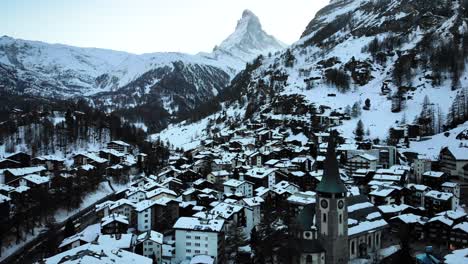 Aerial-flyover-over-Zermatt-city-center-from-the-church-to-river-with-a-view-of-the-Matterhorn-during-winter