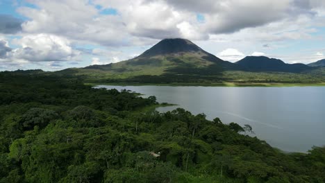 Aerial-view-moving-away-shot,-Scenic-view-of-lake-at-the-foot-of-Arena-Volcano-in-Costa-Rica,-Blue-cloudy-sky-in-the-background