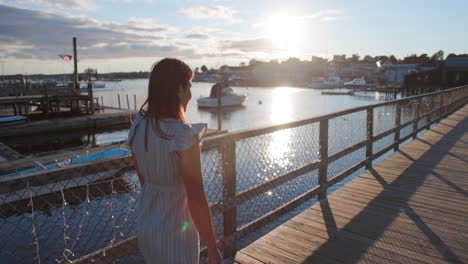 Slow-motion-panning-shot-of-a-young-woman-walking-on-the-Boothbay-Harbor-Footbridge,-a-beautiful-seaside-town