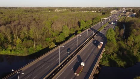 Aerial-panoramic-view-of-busy-highway-over-river-and-surrounded-by-vegetation,-Buenos-Aires