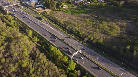 Beautiful-Aeriel-view-of-a-busy-Pilar-highway-at-sunset-surrounded-by-plush-green-vegetation-in-Buenos-Aires,-Argentina