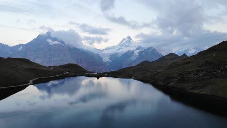 Aerial-flyover-over-lake-Bachalpsee-in-Grindelwald,-Switzerland-at-sunset-with-a-reflection-of-Schreckhorn-and-Wetterhorn-peaks