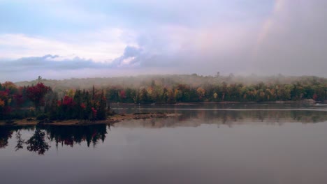 Cottage-Country-in-Fall,-Panning-shot-at-Sunset-with-Cloudy-skies-over-a-Lake-with-Rainbow-and-Mist
