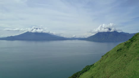 Drone-aerial-footage-of-Guatemalan-volcanos-Volcan-de-Atitlan-and-Volcan-San-Pedro-in-Central-American-highlands-Lake-Atitlan,-Guatemala-surrounded-by-blue-lake-water