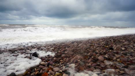 Powerful-stormy-rolling-coastal-ocean-waves-foam-blowing-in-rough-windy-weather-on-pebble-shore