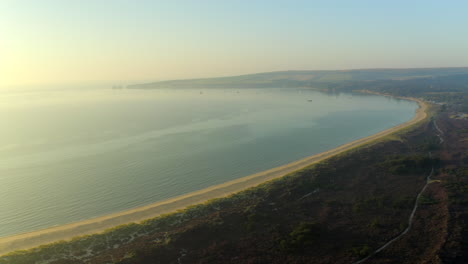 A-sweeping-aerial-shot-of-Studland-Bay-on-the-Dorset-coast-with-views-over-to-Old-Harry-rock's-cliffs-and-a-beautiful-sunrise-and-calm-sea-water