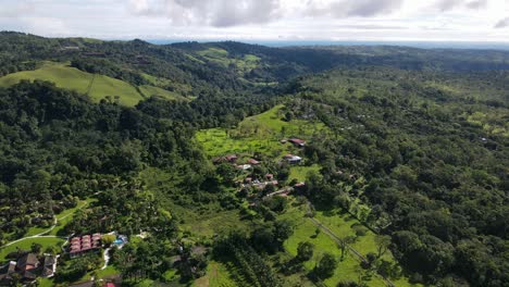 Aerial-view-descending-shot,-Scenic-view-of-a-house-on-top-of-hills-of-La-Tigra-rainforest-in-Costa-Rica,-bright-blue-sky-in-the-background