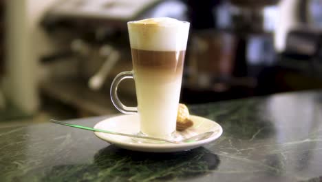 caffe-latte-finished-and-ready-to-be-served-with-a-foam-on-top-and-sweet-on-a-side-in-restaurant-environment-slow-motion