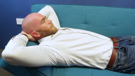 Man-lying-on-a-sofa-relaxing-with-hands-behind-head