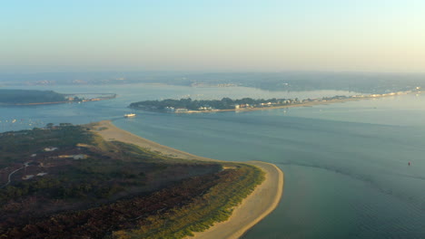 A-sweeping-aerial-shot-of-Poole-Harbour,-Sandbanks,-Brownsea-Island-and-Studland-beach-at-golden-hour-with-calm-peaceful-sea